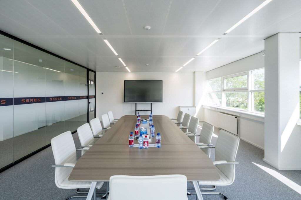 Vergaderruimte aan de Burgemeester Stramanweg met een lange tafel, moderne stoelen, een scherm en flessen water.